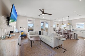 A modern living room with a sectional sofa, a coffee table, and a TV mounted on the wall. - Steele Away by Liquid Life (Gulf Shores)