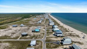 Une vue aérienne d’une zone côtière, avec une rangée de maisons le long de la plage, une route et une vue dégagée sur l’océan.