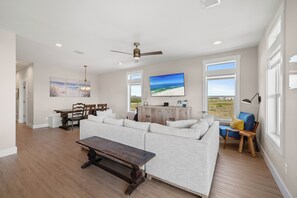 Un salon spacieux avec un canapé d’angle, une table basse en bois et une vue sur l’océan grâce à de grandes fenêtres.