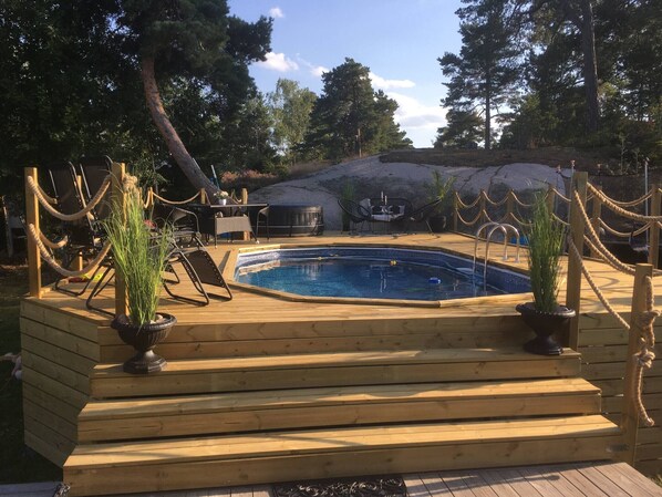 Una terraza de madera con piscina, rodeada de árboles y un muro de roca.