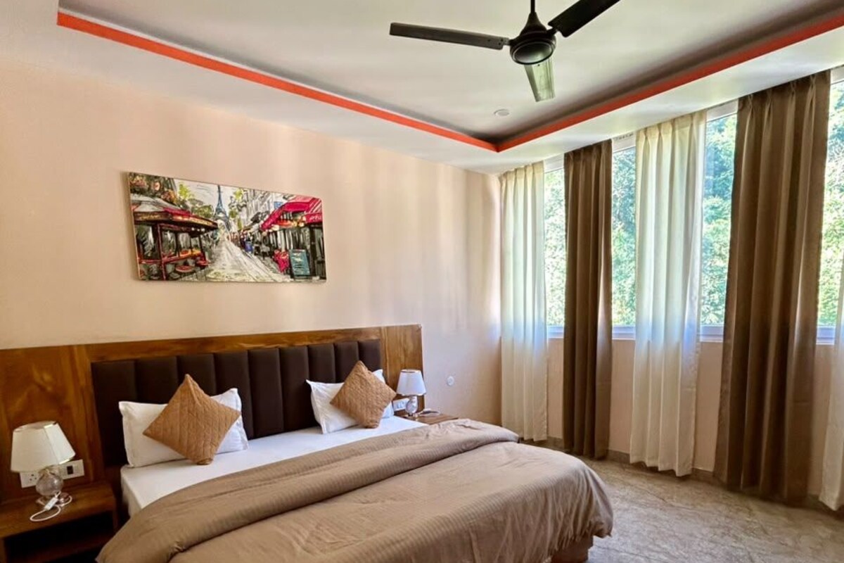 Quarto de hotel com uma cama grande, um ventilador de teto, um quadro na parede e uma janela com cortinas.