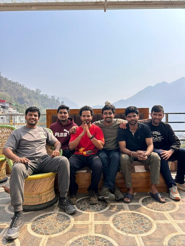 A group of people sitting on a wooden bench with a patterned floor, overlooking a mountainous landscape. - Namaste Hostel Rishikesh (Rishikesh)