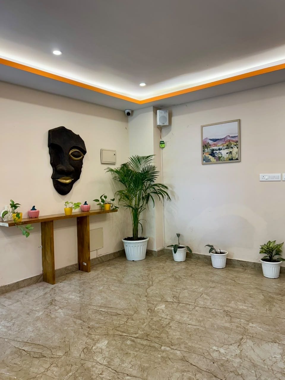 A reception area with a marble floor, a wooden reception desk, a large potted plant, a wall-mounted artwork, and a ceiling with recessed lighting.