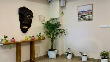 A reception area with a marble floor, a wooden reception desk, a large potted plant, a wall-mounted artwork, and a ceiling with recessed lighting.