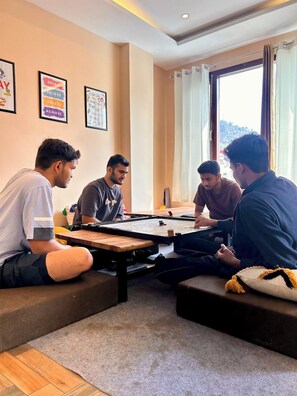A group of people playing a board game in a room with a large window, a wooden table, and motivational posters on the wall. - Namaste Hostel Rishikesh (Rishikesh)