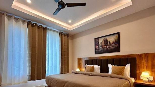 A modern bedroom with a large bed, a ceiling fan, and a nightstand with a lamp. - Namaste Hostel Rishikesh (Rishikesh)