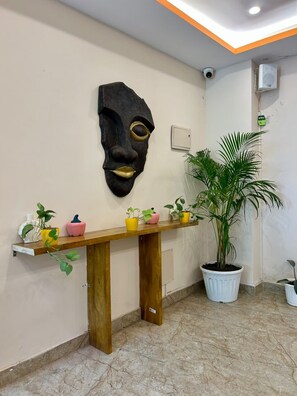 A reception area with a wooden reception desk, a large potted plant, and a wall-mounted decorative mask.