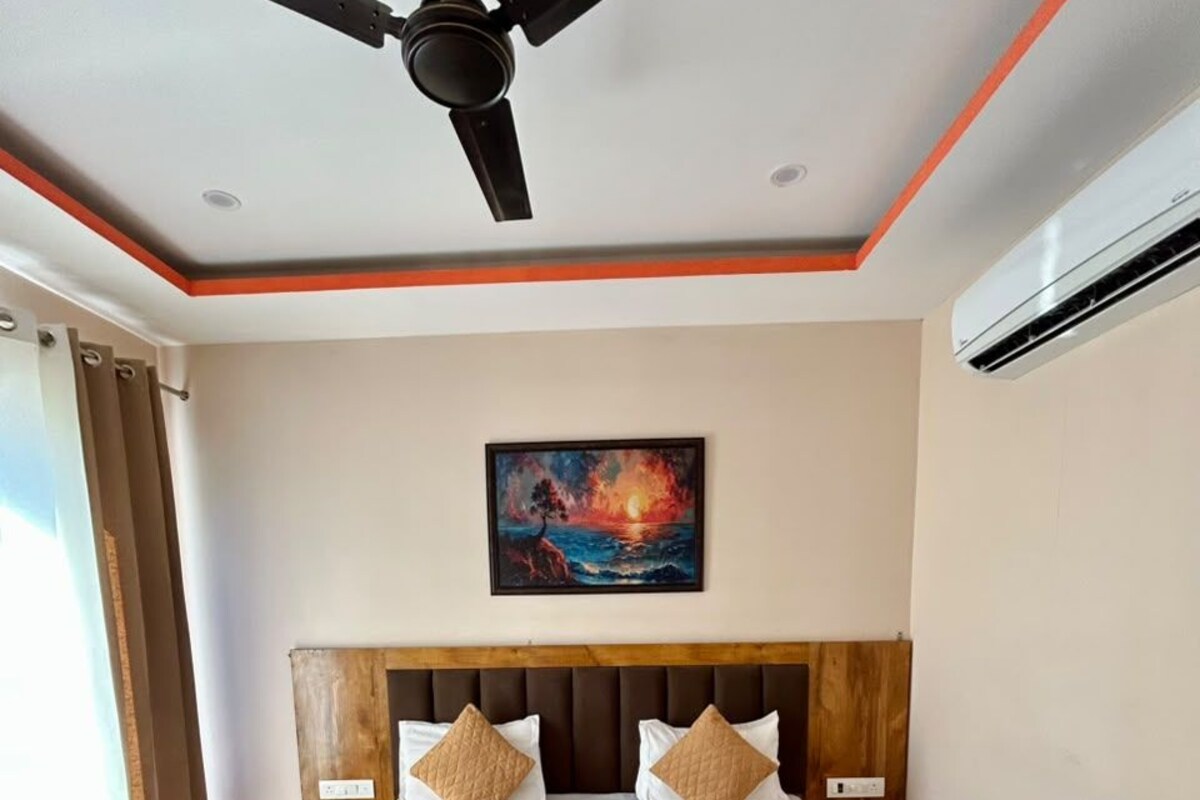 Quarto de hotel com uma cama grande, ventoinha no teto, aparelho de ar condicionado e um quadro na parede.