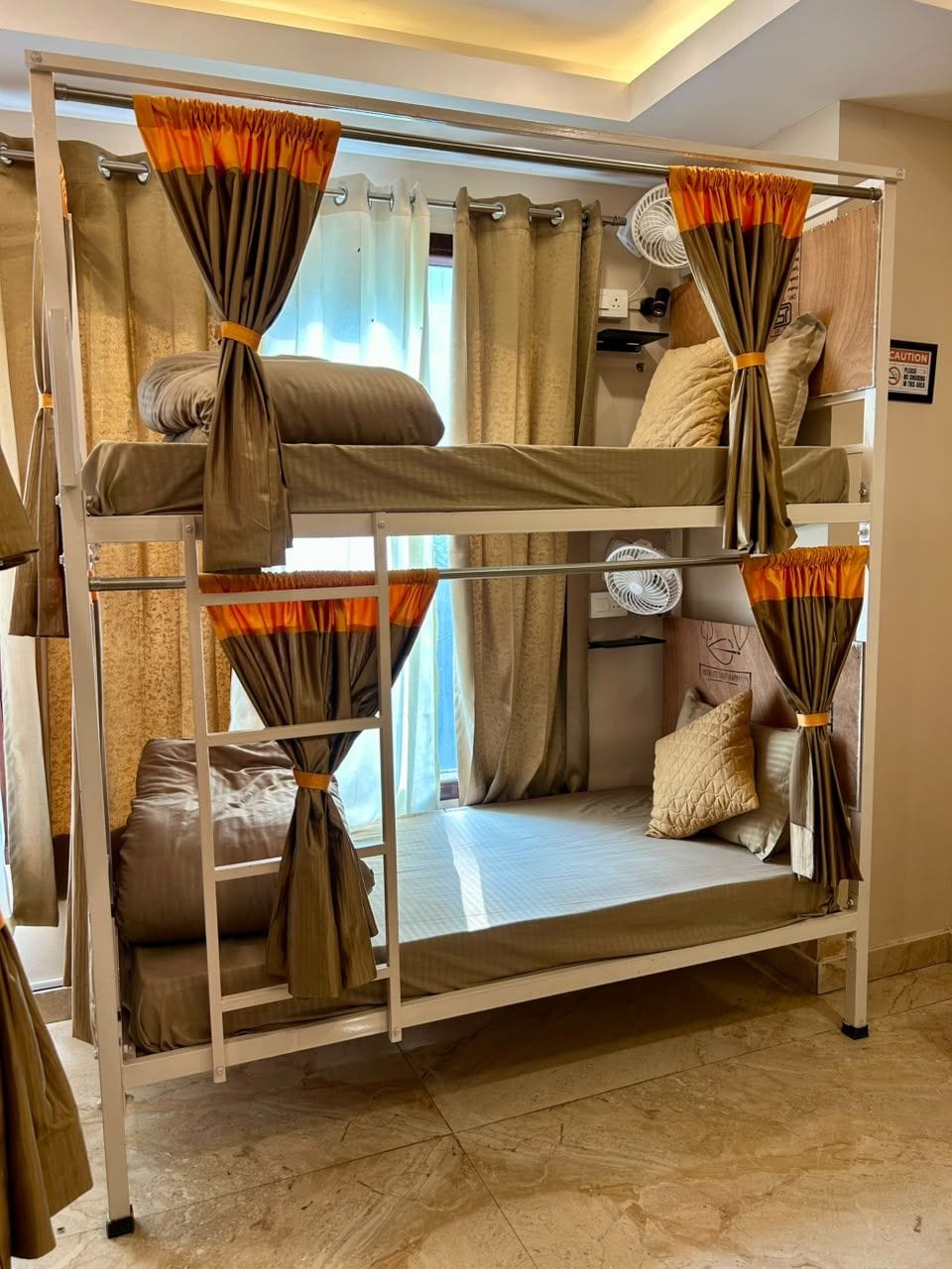 Una cama individual con cortinas, un ventilador y un almohadón en la cama inferior.