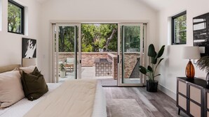 A bedroom with a bed, a nightstand, a lamp, and a view of an outdoor patio. - Furnished Modern Luxury Retreat (Austin)