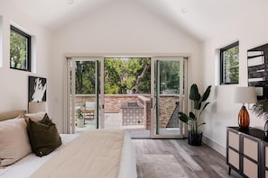 Ein Schlafzimmer mit Bett, Nachttisch, Lampe und Blick auf eine Terrassengartenanlage.
