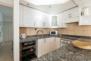 A kitchen with white cabinets, a granite countertop, a microwave, and a sink. - Club Villamar Exclusive Beachfront Penthouse (Costa Adeje)