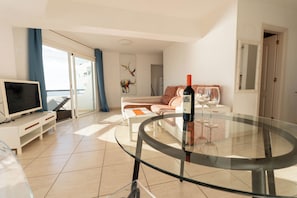 A modern living room with a glass table, a sofa, a TV, and a wine bottle. - Club Villamar Exclusive Beachfront Penthouse (Costa Adeje)