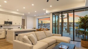 En moderne stue med en beige sofa, et sofabord og udsigt til bybilledet gennem store vinduer.