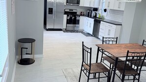 A modern kitchen with white cabinets, stainless steel appliances, and a dining area with a wooden table and chairs. - Large 5BR Home Sleeps 12 Fireplace  ADA-Friendly Access (Halethorpe)