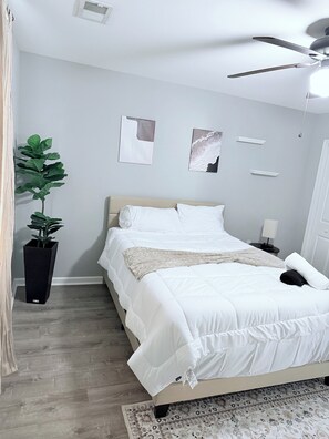 Een keurig opgemaakte slaapkamer met een bed, een potplant en een plafondventilator.