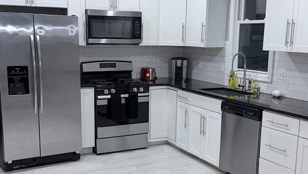 A modern kitchen with white cabinets, stainless steel appliances, and a herringbone-patterned floor. - Large 5BR Home Sleeps 12 Fireplace  ADA-Friendly Access (Halethorpe)