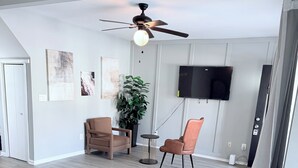 A modern living room with a ceiling fan, a flat-screen TV mounted on the wall, a potted plant, two leather chairs, and a glass coffee table. - Large 5BR Home Sleeps 12 Fireplace  ADA-Friendly Access (Halethorpe)