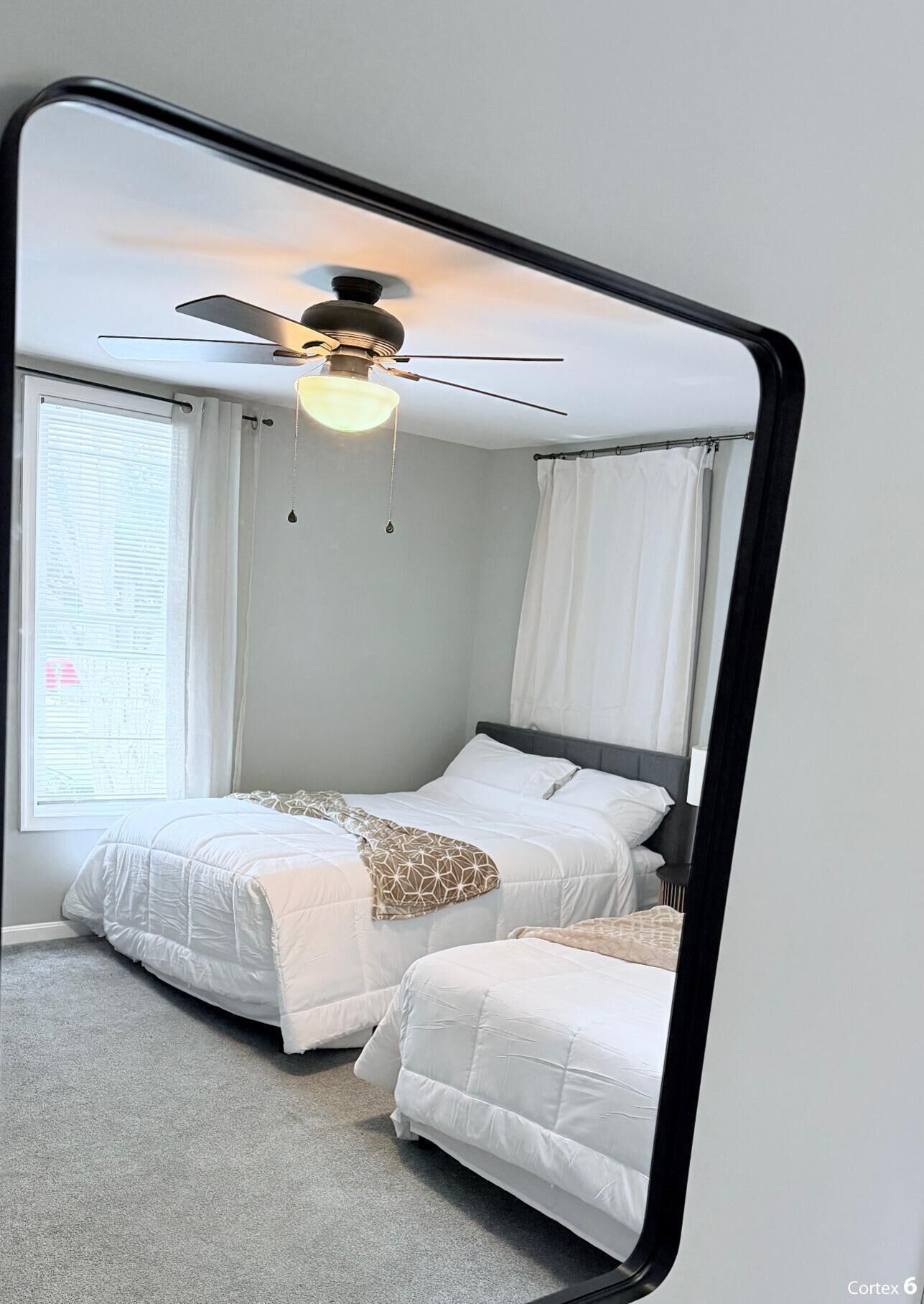 A bedroom with two beds, a ceiling fan, and a large mirror reflecting the room.
