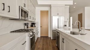 A modern kitchen with white cabinetry, stainless steel appliances, and a wooden floor. - Pearl Beach B: Lagoon Front + Beach Access (St. George)