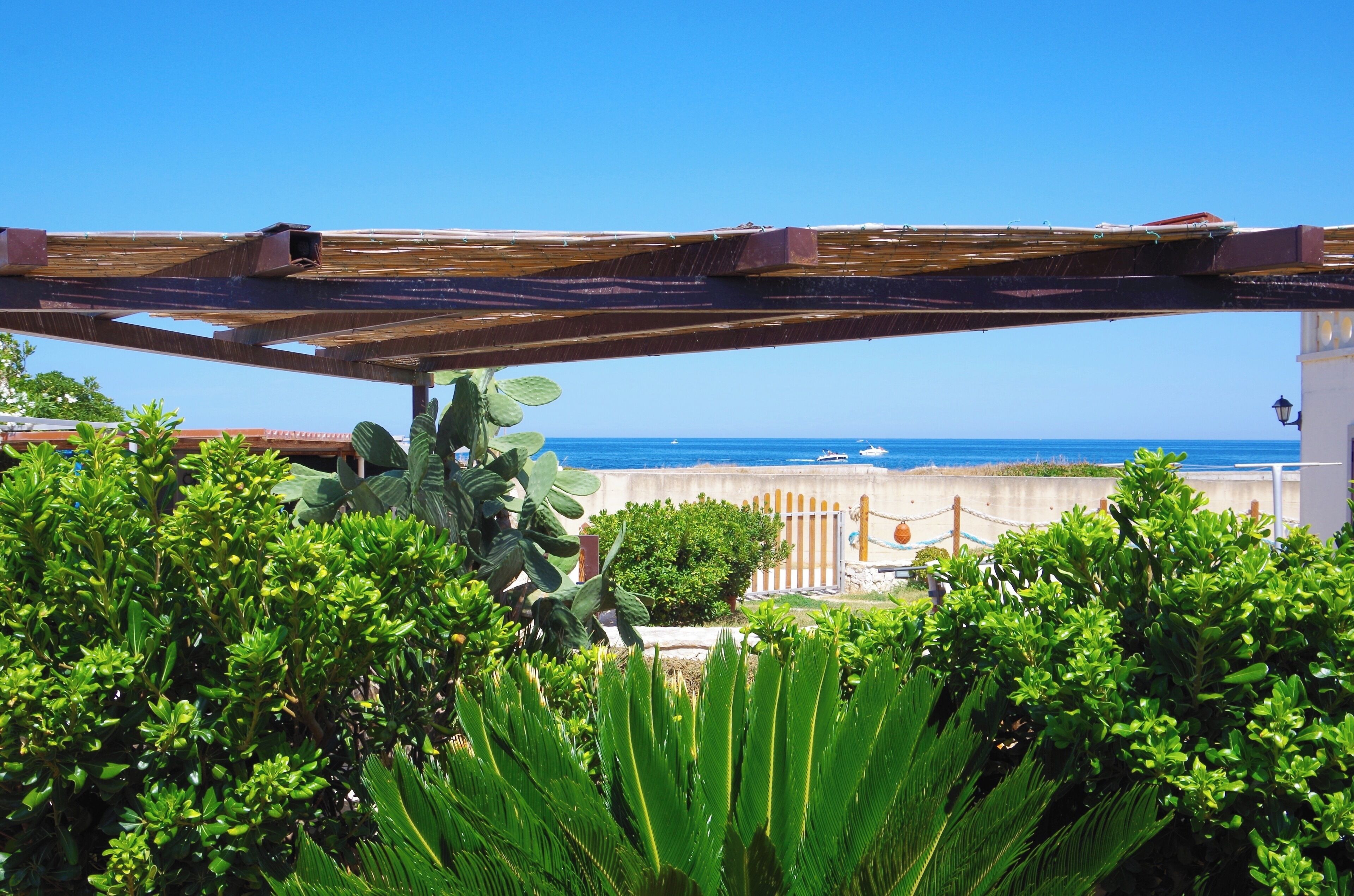 A wooden pergola with a view of the sea and a white building in the background.