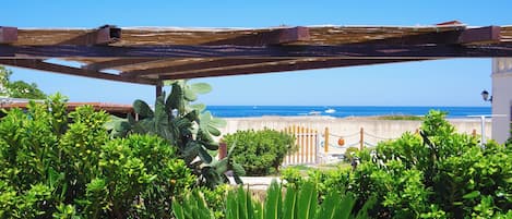 A wooden pergola with a view of the sea and a white building in the background.