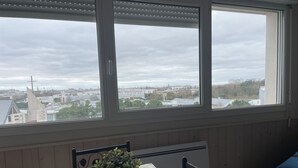 Ein Zimmer mit Tisch und Stühlen, einer Topfpflanze auf dem Tisch und Blick auf Gebäude durch große Fenster.