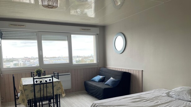 Ein Zimmer mit einem Bett, einem Tisch mit Stühlen, einem Fenster mit Jalousien und einem runden Spiegel an der Wand.