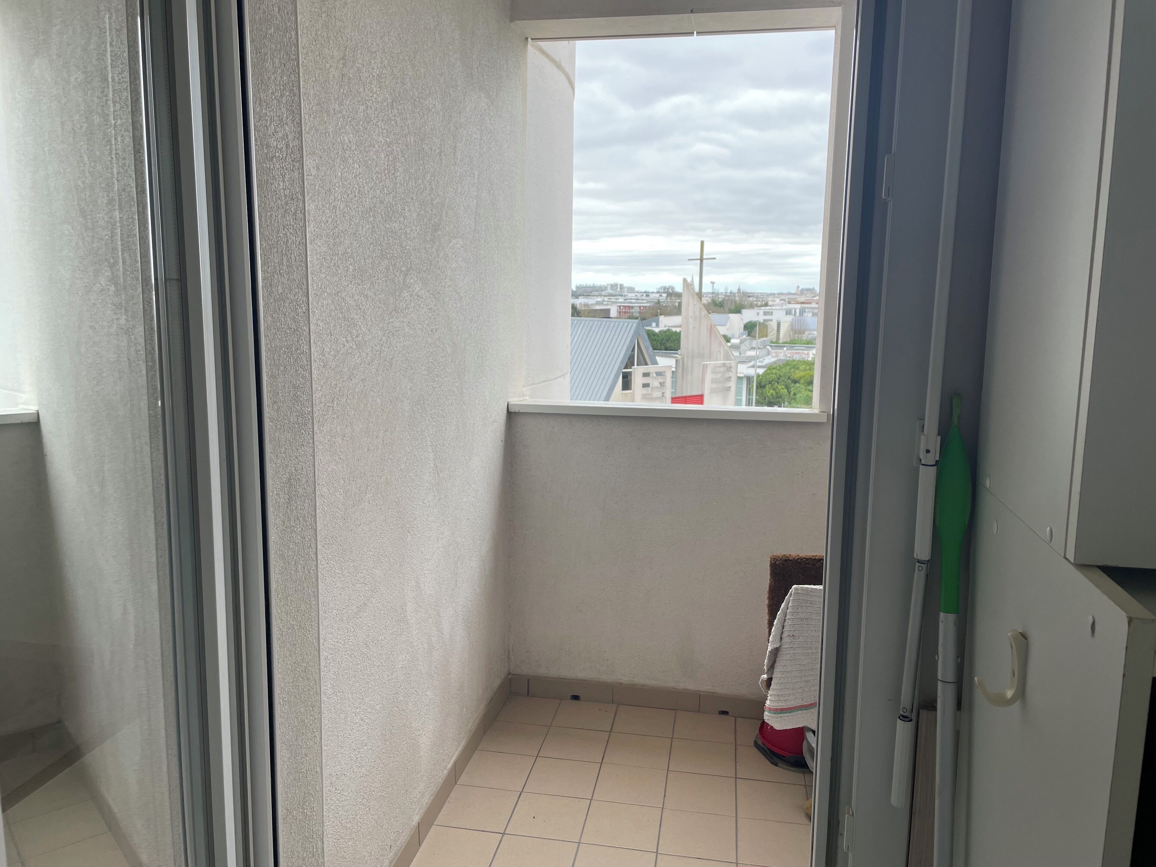 Un pequeño balcón con vistas a un paisaje urbano, suelo de baldosas y una puerta con una toalla colgada.