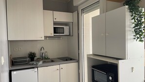 Eine kleine Küche mit weißen Schränken, einer Mikrowelle, einem Spülbecken und einem kleinen Fenster.