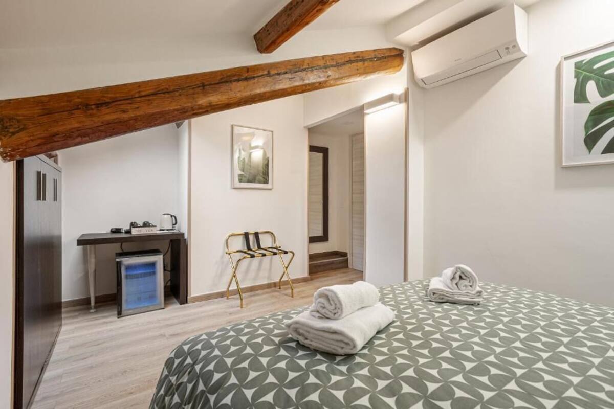 A hotel room with a bed, a desk, a chair, and an air conditioning unit.