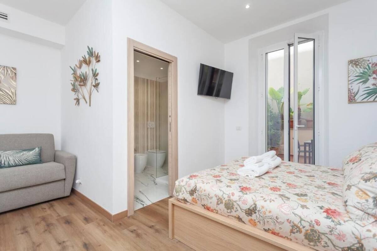 A bedroom with a bed, a sofa, a TV, and a door leading to a balcony.