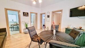 A modern living room with a round dining table, two chairs, a sofa, and a TV mounted on the wall.