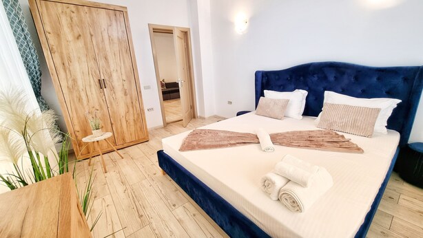 A bedroom with a large bed, wooden wardrobe, and a small round table with a plant.