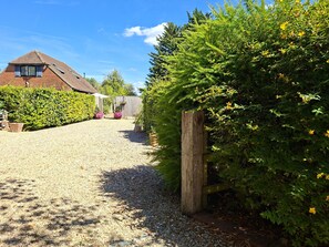 A gravel driveway leading to a house with a sloped roof, surrounded by dense greenery and a wooden fence. - Dandydills -  an annexe that sleeps 2 guests  in 1 bedroom (Colworth)