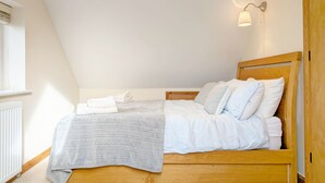 Un dormitorio con techo inclinado, estructura de cama de madera, mesita de noche, lámpara de pared y radiador.
