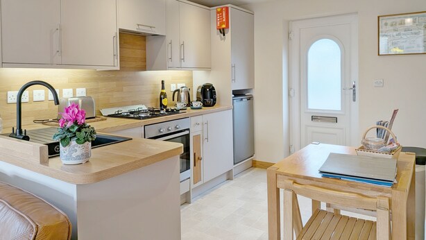 Una cocina moderna con una isla central, horno empotrado y un comedor con mesa y banco de madera.