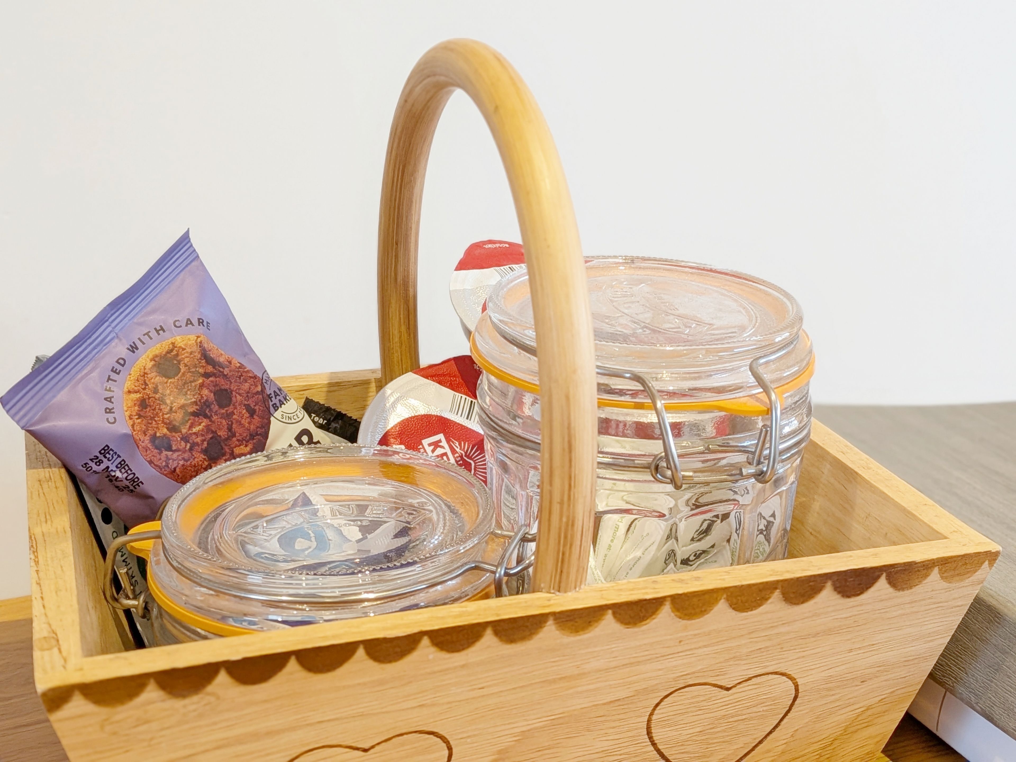 A wooden basket containing glass jars, a packet of cookies, and a KFC box.