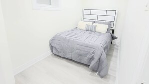 A small, well-lit bedroom with a single bed, a window, and a plain white wall. - Niagara Cozy Suite - Modern 2bed 15 min to Falls (Thorold)