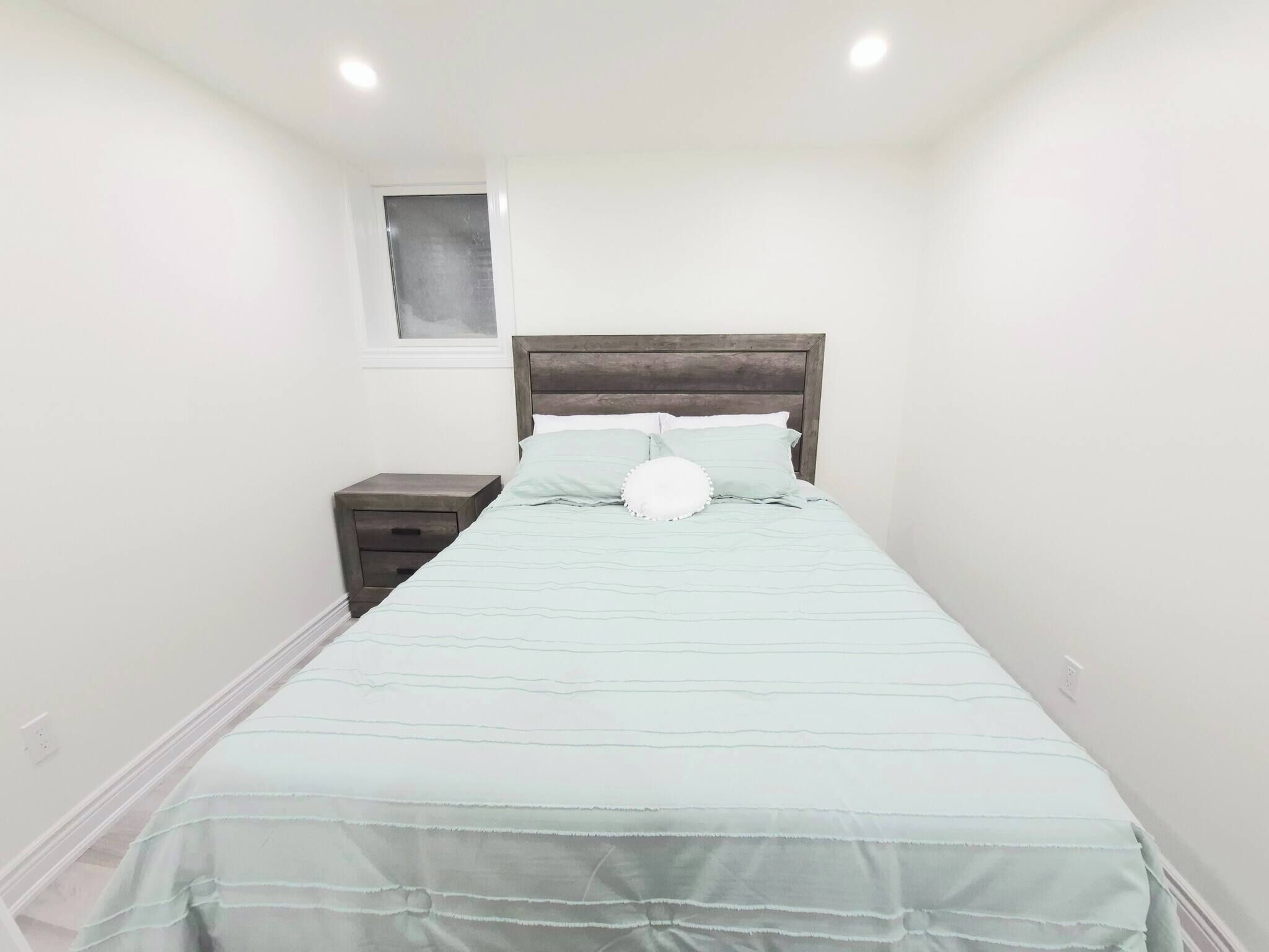 A bedroom with a bed, nightstand, and a window.
