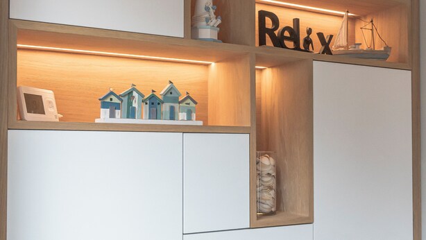 A modern room with a wooden cabinet, a shelf with a ship model, and a 'Relax' sign.