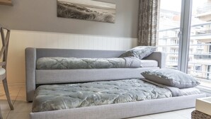 A modern bedroom with a grey sofa bed, a large window with curtains, and a city view.