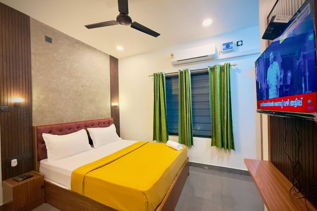 A hotel room with a bed, a ceiling fan, an air conditioning unit, and a television on the wall.