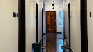 A hallway with a wooden door at the end, a trash bin, and a bench. - NAKSHATRA (Neyyattinkara)