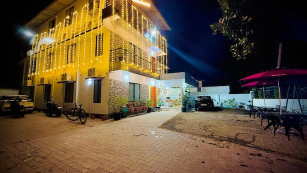 A building with a sign reading "NAKSHATRA" at night, featuring a paved entrance, parked vehicles, and outdoor seating. - NAKSHATRA (Neyyattinkara)
