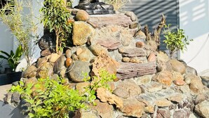 A stone statue of a seated figure on a rock formation, surrounded by greenery and a tree. - NAKSHATRA (Neyyattinkara)