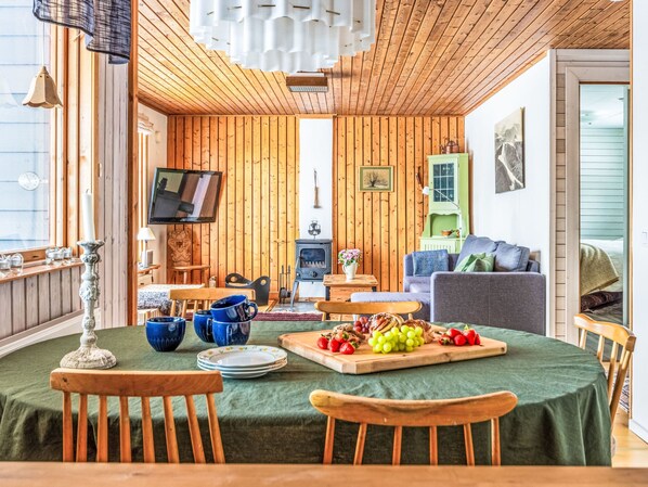 Una habitación acogedora con paredes de madera, un televisor, un sofá verde y una zona de comedor con una mesa lista para una comida.