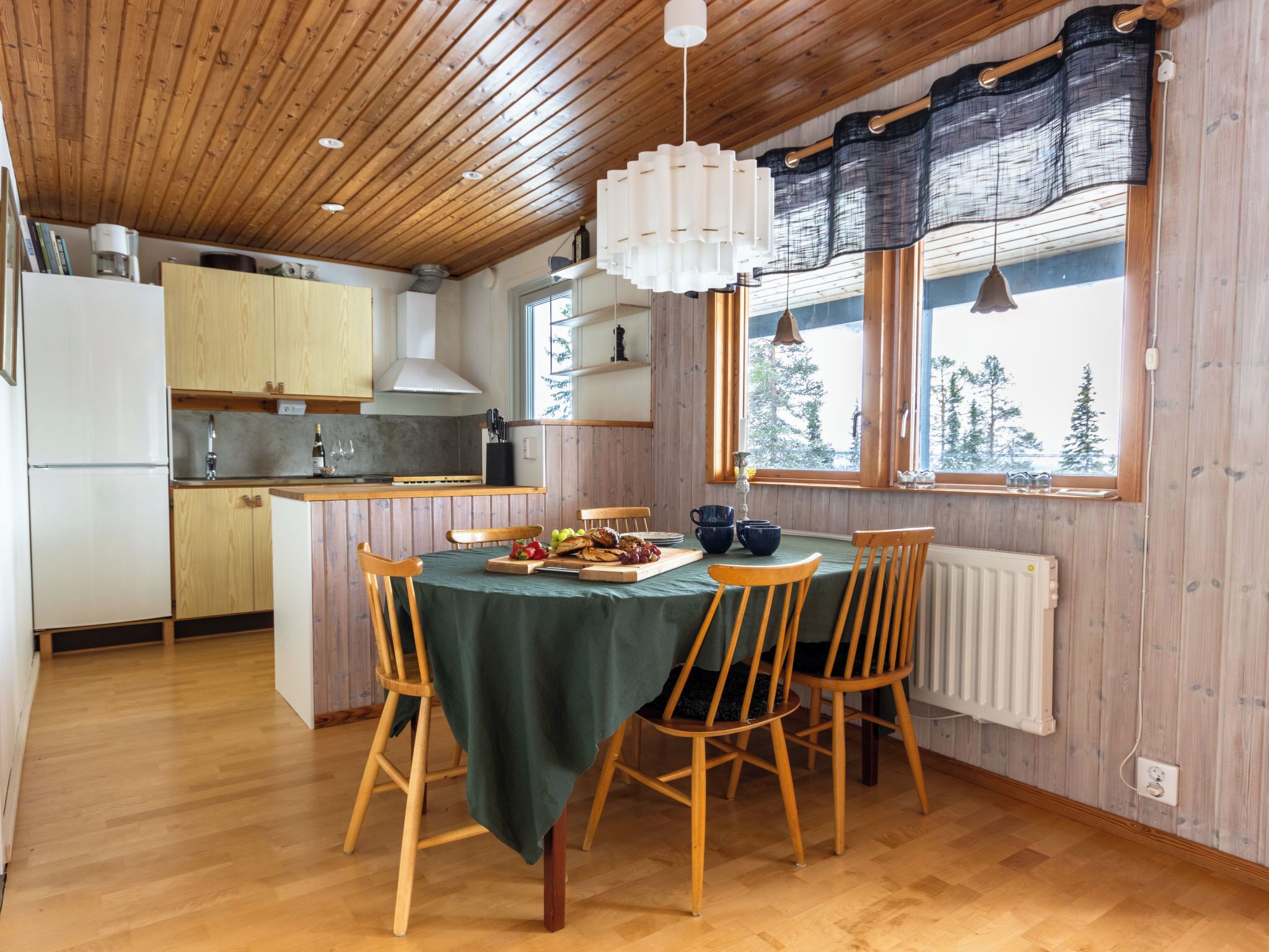Un interno in legno con tavolo da pranzo, sedie, angolo cottura e finestra vista alberi.