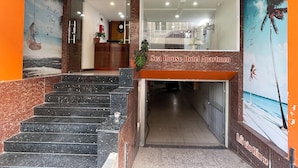 Entrada de un hotel con una escalera que lleva a una zona de recepción, un espejo grande y una pared con un mural tropical.