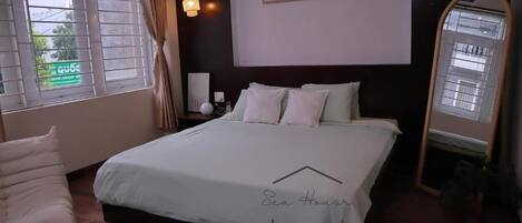 Un dormitorio de hotel con una cama, una mesita de noche, un espejo y una ventana con cortinas.